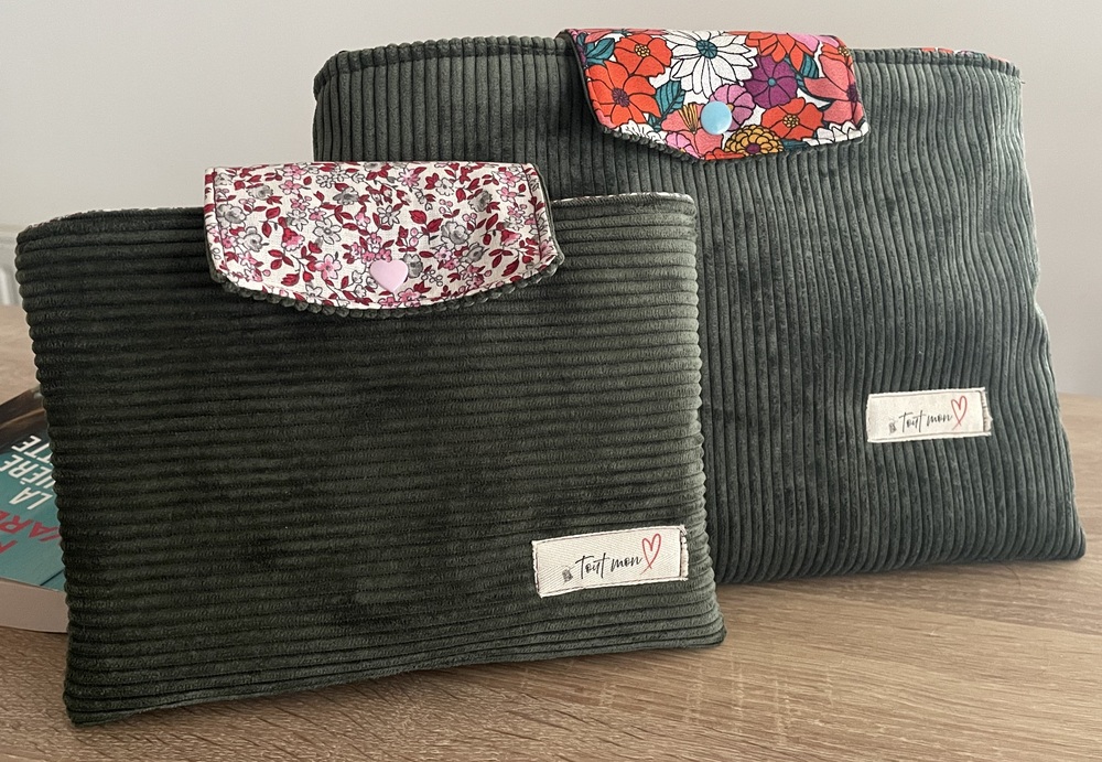 Deux pochettes à livre en velours côtelé kaki posées côte à côte : l'une avec rabat fleuri rose et gris, l'autre avec rabat à grandes fleurs colorées rouges, blanches et violettes