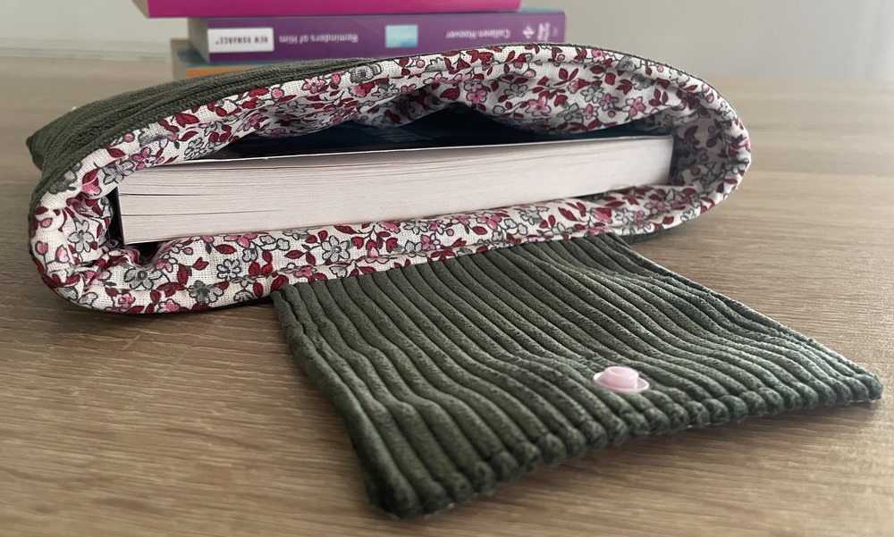 Pochette à livre en velours côtelé kaki ouverte, révélant sa doublure en tissu fleuri rose et gris avec un livre glissé à l'intérieur