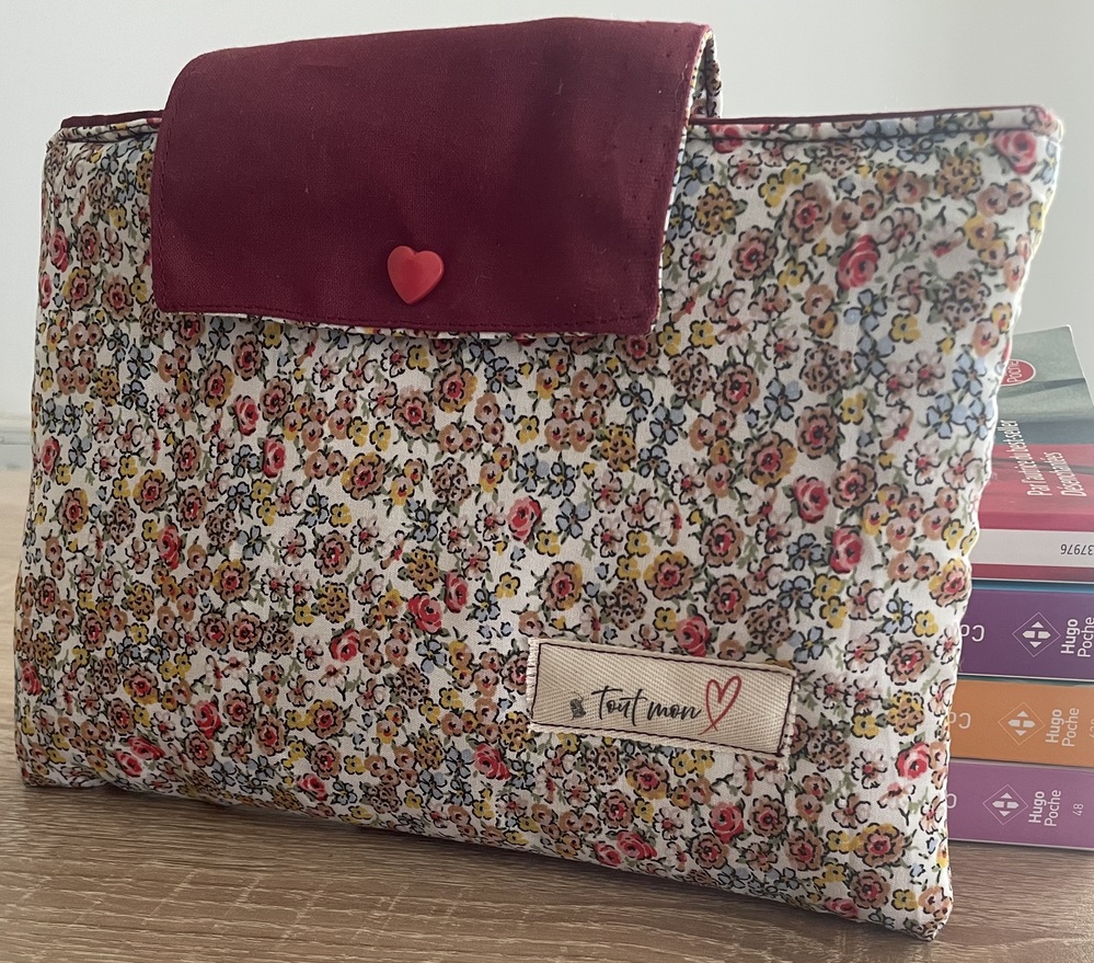 Pochette à livre en tissu liberty à petites fleurs multicolores roses, jaunes et bleues sur fond blanc, avec rabat en velours bordeaux et bouton cœur rouge